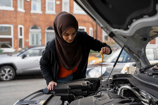 Woman wearing hijab checking oil in car engine