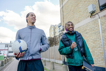 Young male friends with football walking outdoors