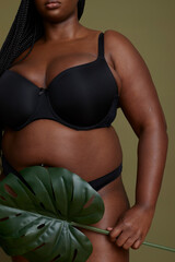 Woman in underwear with monstera leaf against green background