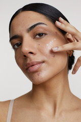 Studio shot of young woman applying cream on face