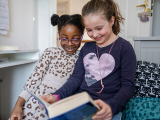 Girl friends (6-7) reading book at home