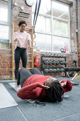 Daughter helping mother practicing sit-ups in gym