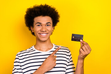 Portrait of young guy wear striped t-shirt directing finger new debit banking card online pay system isolated in yellow color background