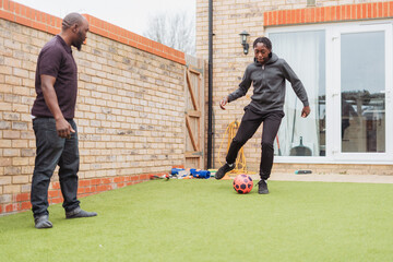 Father playing soccer with teenage son (14-15) in backyard