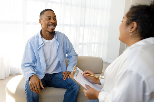Cheerful african guy smiling to young woman psychotherapist