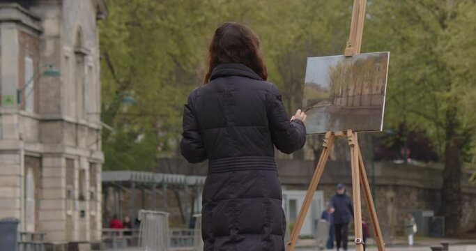 Woman painting a picture near the river Seine. Creative woman artist paints a picture with a brush while standing near the easel in Paris. Woman artist, art for sales, inspiration