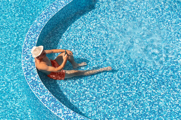 Young man relaxing in resort hotel swimming pool, using smartphone, during summer holidays. Tourist...