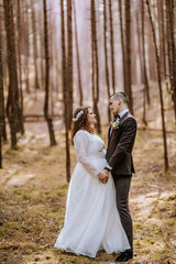 bride and groom standing in a pine forest in spring sunny day, couple wedding