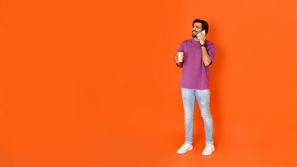 Fototapeta na wymiar Cheerful indian man using smartphone, have phone call, drinking coffee