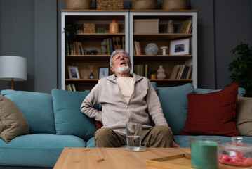 Aged grey haired senior red face man writhes in pain suffers from low back strain, touch rubbing or...