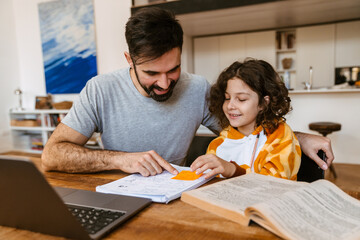 Father helping his son with homework while sitting with laptop at table