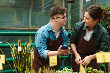 Man with down syndrome and woman florist smiling while working together in greenhouse