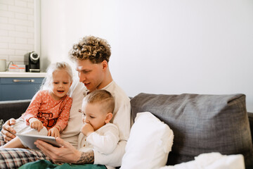 Father and his kids watching cartoons on digital tablet while sitting on couch