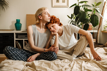 Gay couple in love hugging while sitting on bed