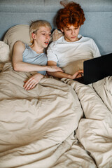 Gay couple in love using laptop while laying in bed