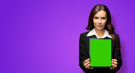 Naklejka premium Portrait of serious brunette businesswoman showing tablet pc, touchpad, with green chroma key screen, on violet purple background. Confident attractive business woman at office.