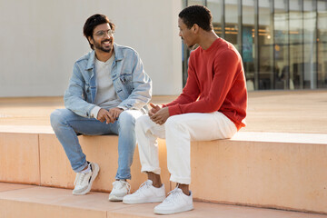 Cheerful arab and black millennial student and teacher man in casual talking, preparing for test
