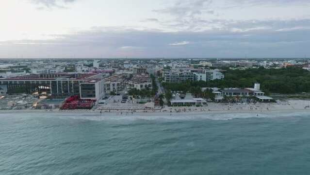 Aerial drone dolly in view of a cityscape by the coast, with built structures, rolling clouds and endless horizon in Playa del Carmen, Mexico.