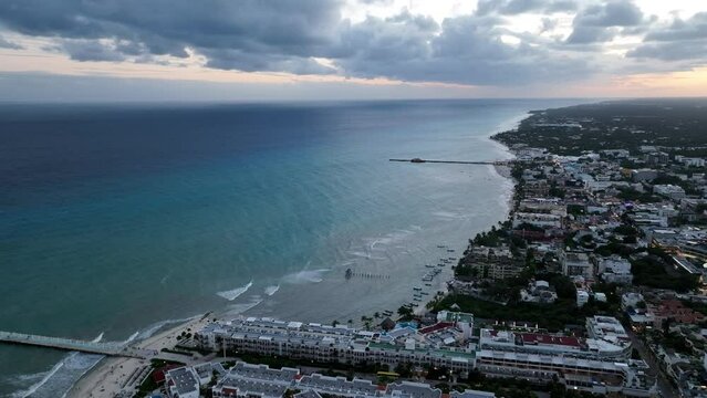 A stunning aerial view of a cityscape by the coast, with built structures, rolling clouds and endless horizon on magic hour in Playa del Carmen, Mexico.