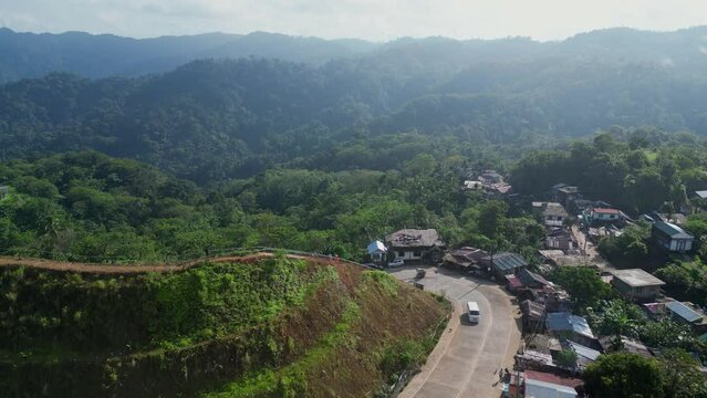 Idyllic Aerial View of a Philippine mountainside village town with winding roads and facing a vast, tropical rainforest during summertime. Viga, Catanduanes.