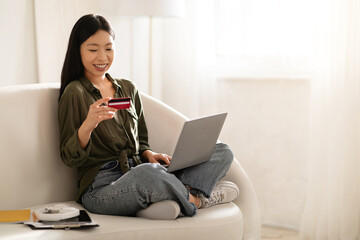 Smiling asian woman using laptop and bank card at home