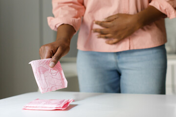 Classic comfort of menstrual pads. Black woman taking sanitary napkin from table, suffering from...