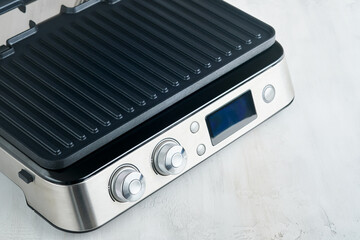 Obraz premium Electric grill. Modern kitchen portable grill tool for modern kitchen for grilling meat, vegetables and snacks for dinner or party on light gray background. Place for text or advertisement. Mock up.