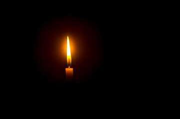 A single burning candle flame or light glowing on an orange candle on black or dark background on...