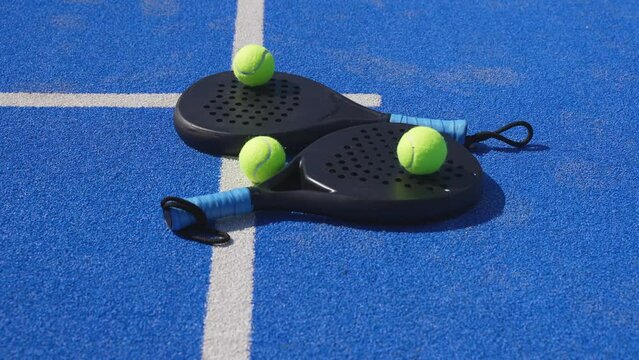 Padel rackets and two yellow balls on the court.