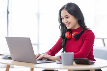 Beautiful Young asian woman at home sitting on the sofa while using laptop and headphone at home