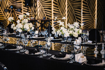 Banquet decoration composition flowers, candles, candlesticks in hall restaurant. Luxury wedding reception. Table setting, setup. Trendy black rich decor. Birthday, baptism, event. Details interior.