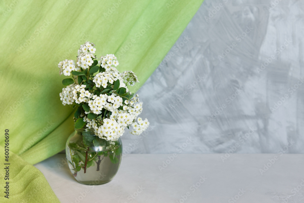 Wall mural Fresh summer bouquet of white flowers in vase on a gray shelf against a gray loft wall. Decor with a green textile curtain. Floral home decor.	