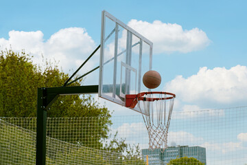 Naklejka premium Basketball ball flies into the ring. Outdoor sports ground for playing basketball. Sports activities in city parks.