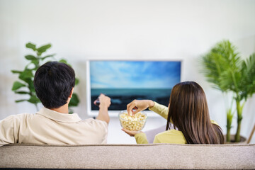 Asian family Watching smart TV together and using remote controller Hand holding popcorn at home with the remote control movie or TV series spending time at home - Powered by Adobe