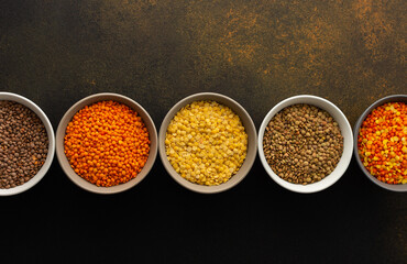 Multicolored lentils in bowls on a brown background, yellow and brown, green and orange lentils, healthy legumes, top view, copy space
