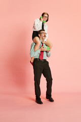 Portrait with couple, shocked man and emotional woman sitting on male shoulders speaking via telephone and shouting over pink studio background