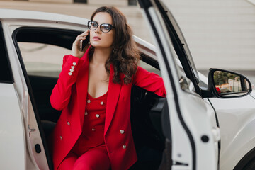 beautiful sexy rich business woman in red suit sitting in white car, wearing glasses