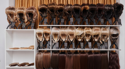 Showcase of natural looking wigs in different colors fixed on the metal wig holders in beauty salon. Row of mannequin heads with variation shades hair on shelf in wig shop.