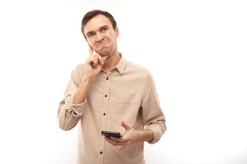 Portrait of young handsome caucasian man using mobile phone with thoughtful face isolated on white studio background, pensive facial expression