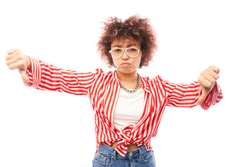 Portrait of displeased young brunette curly woman showing thumbs down isolated on white studio background. Does not approve of something, puts a dislike