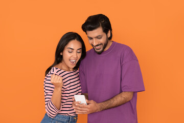 Naklejka premium Emotional eastern lovers using cell phone and gesturing on orange