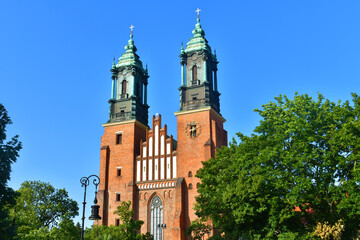 Fototapeta na wymiar Catholic church with green top of cathedral towers in the background of blue sky, trees around. A sunny summer day. Cathedral on the Tymsky island. Poland, Poznan, June 2022.