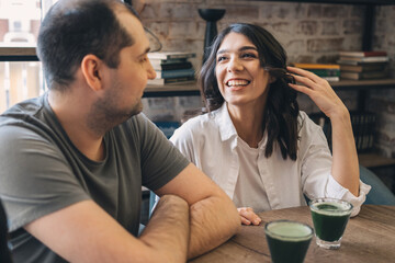 Fototapeta premium A happy man and a woman are talking in a cafe.Glasses of matcha tea on the table.Communication, healthy eating concept.