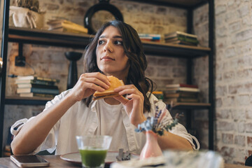 Portrait of a young attractive dark-haired woman eating a sandwich in a cafe.