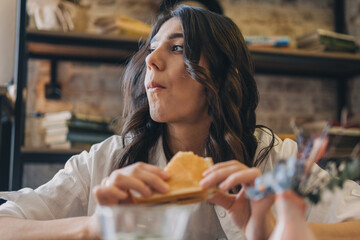 Portrait of a young attractive dark-haired woman eating a sandwich in a cafe.