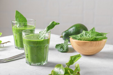Healthy green smoothie with spinach, avocado, banana, and vegan milk in two glasses and fresh ingredients on light grey table background. Detox, diet, healthy, vegetarian food concept