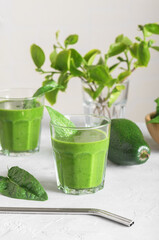 Healthy green smoothie with spinach, avocado, banana, and vegan milk in two glasses and fresh ingredients on light grey table background. Detox, diet, healthy, vegetarian food concept