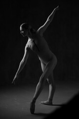 Ballerina in a beige bodysuit and pointe shoes. Dark background. Sculpted beautiful female body. Pose of a gymnast.