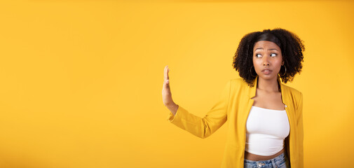 Serious african american lady doing stop gesture with hand and looking aside at free space, yellow background, panorama