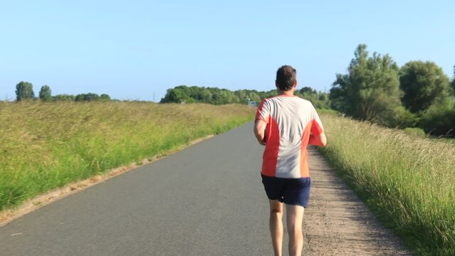 Male trail runner on floodplains valley dyke. Athlete endurance training run exercise outdoor sports workout concept. Steady shot of person in motion